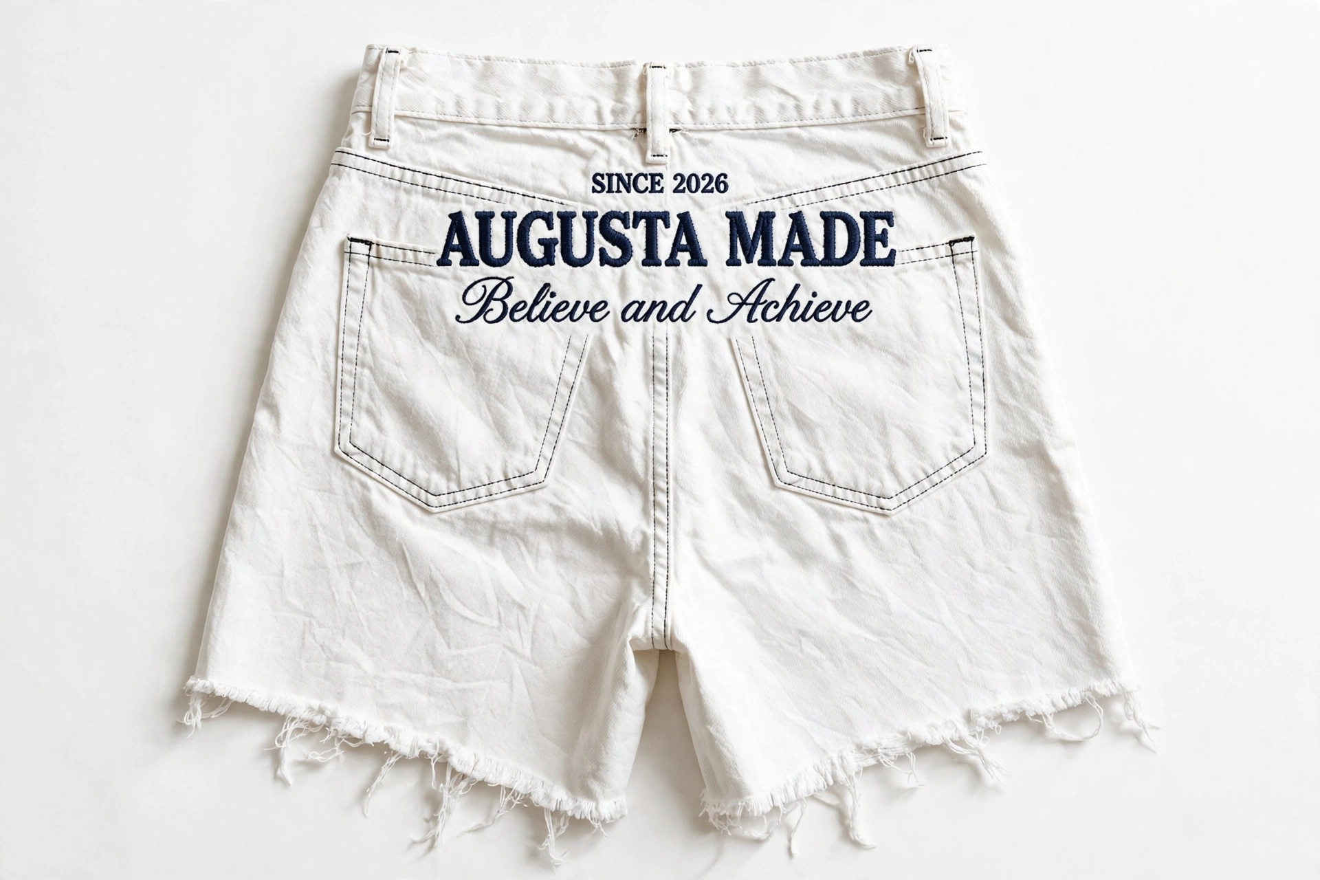 Back of white cutoff denim daisy dukes embroidered with Since 2026, Augusta Made, Believe and Achieve